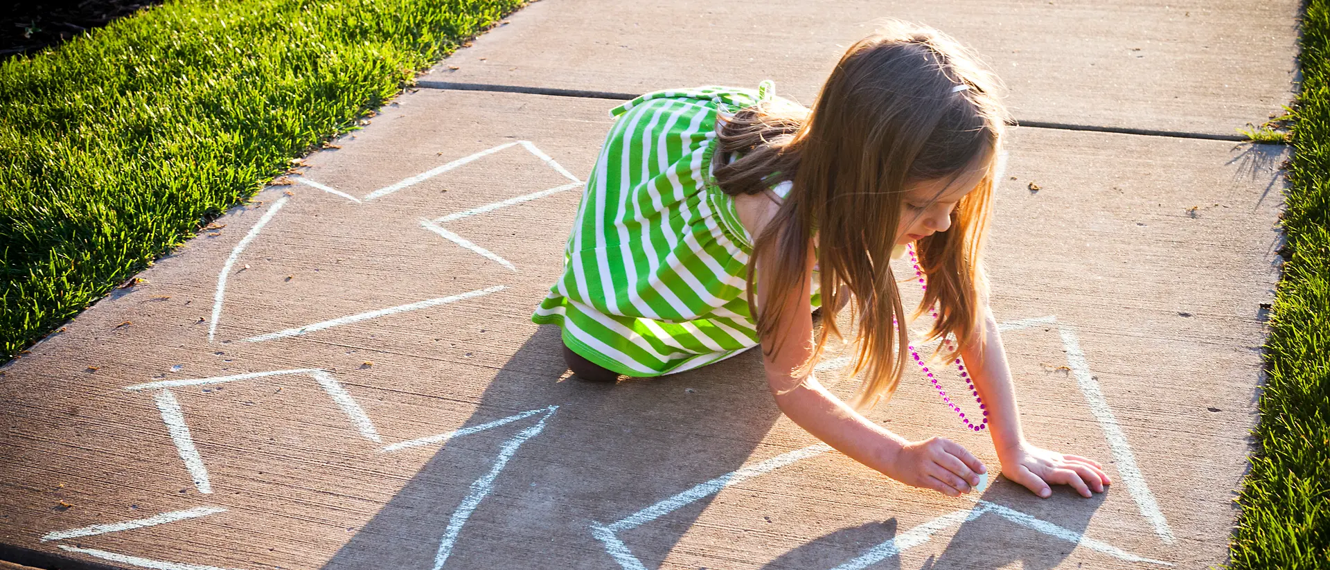 Niña con vestido verde pintando flechas con tiza en un camino.