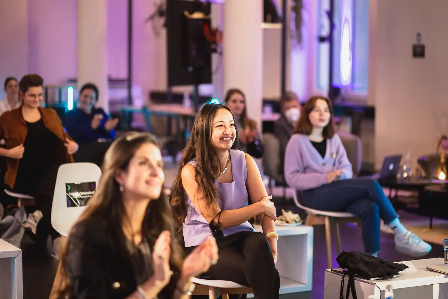 Several female founders sitting together in the audience, captivated, looking ahead.