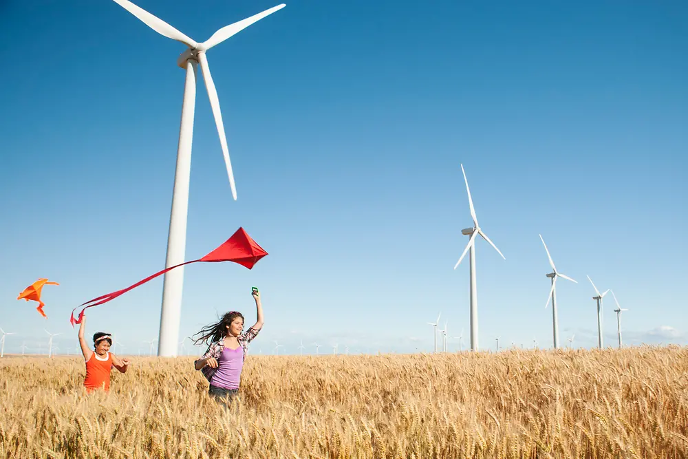 Niños jugando con una cometa en un campo delante de molinos de viento.