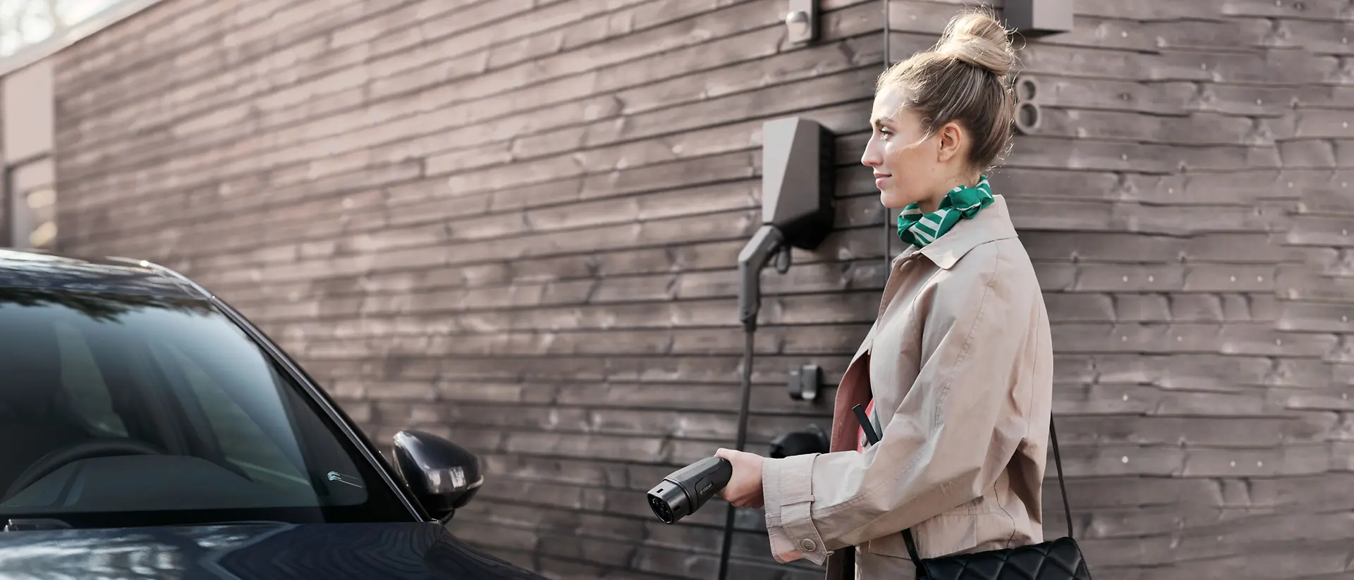 Una mujer al lado de un coche eléctrico con el cable de carga.