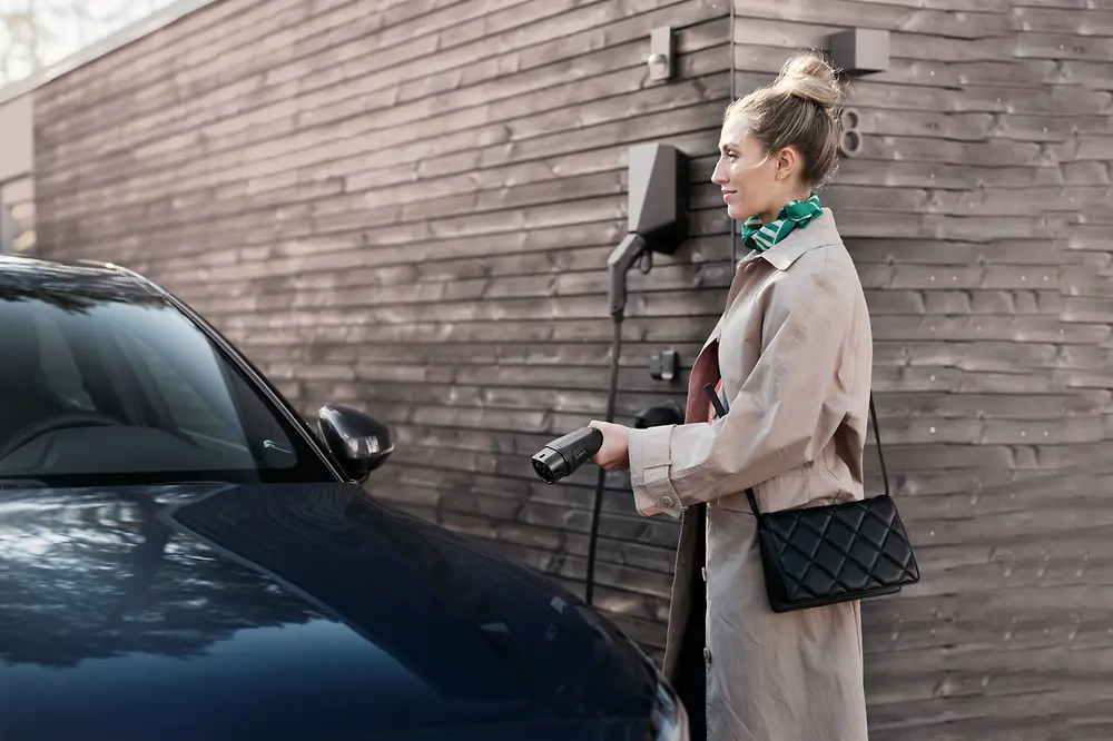 Una mujer al lado de un coche eléctrico con el cable de carga.