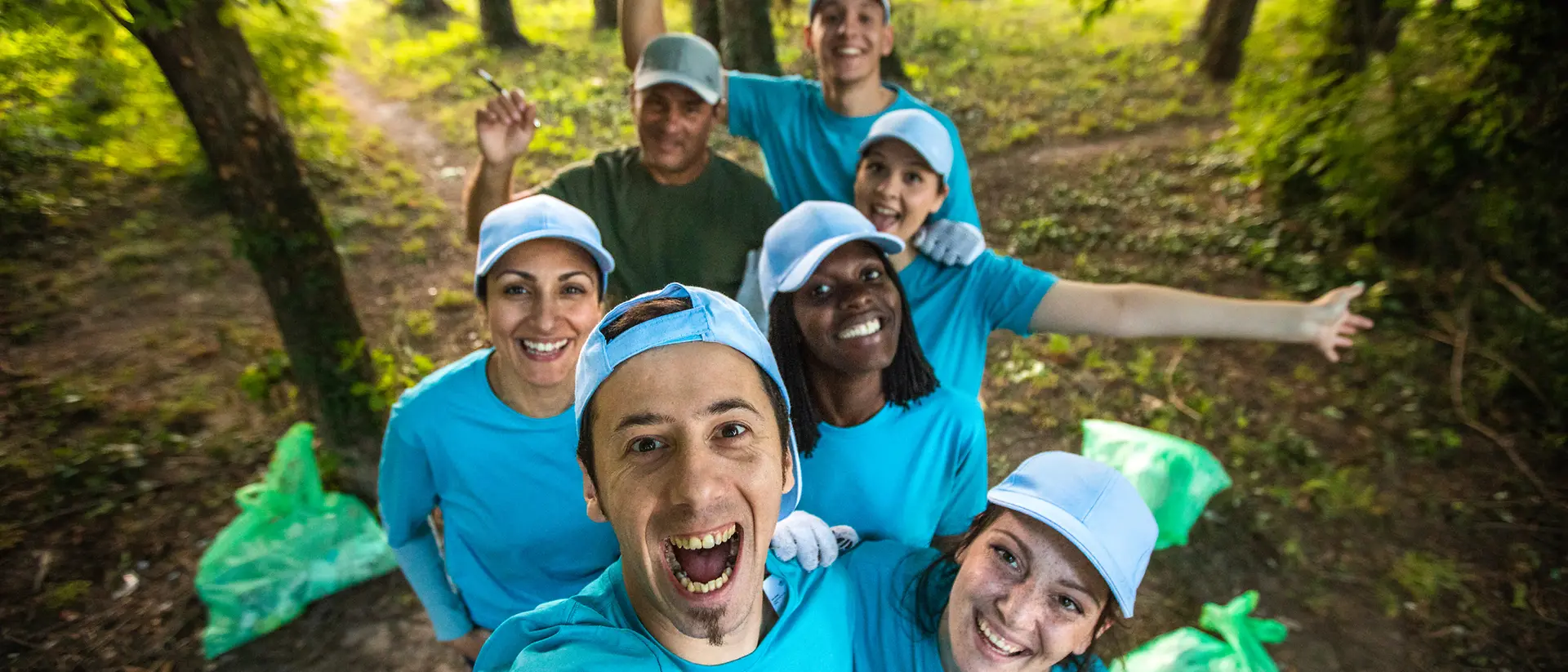 Un grupo de voluntarios se toma una selfie en el bosque con bolsas de basura llenas a su lado.