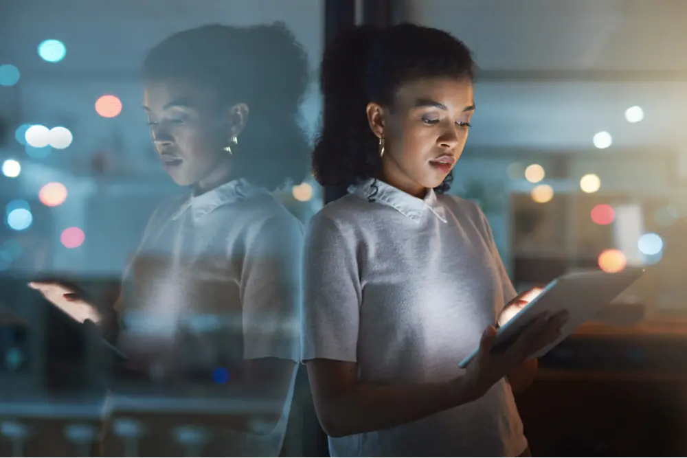 Mujer con iPad de pie frente a una ventana oscura.