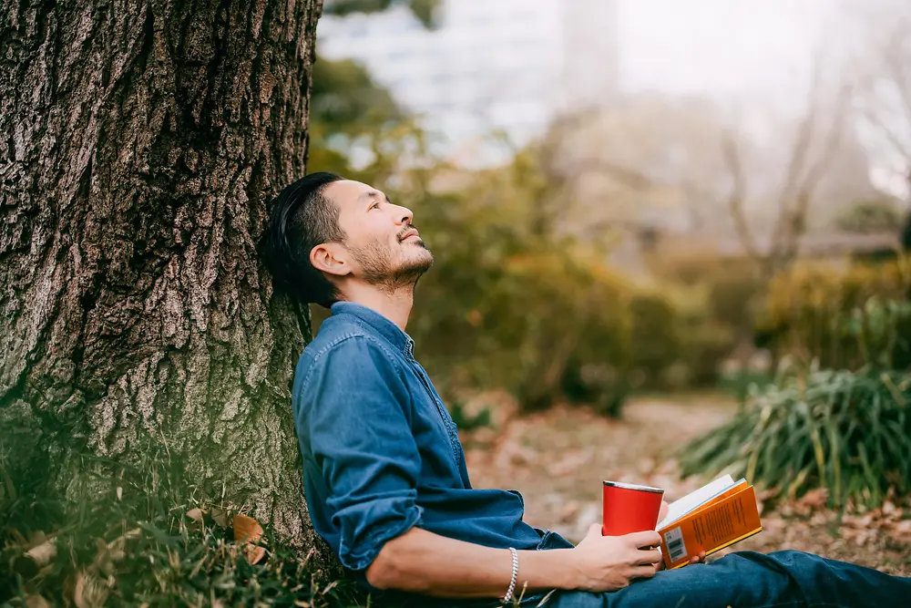 Un hombre apoyado en un árbol con un libro